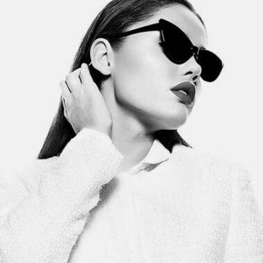 A woman wearing sunglasses and holding her hand to the side of her head.